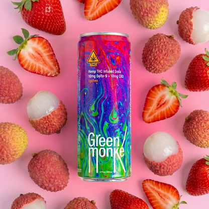 A colorful can of Green Monkey hemp THC-infused soda is centered on a pink background, surrounded by fresh strawberries and lychees. The can features a vibrant, multicolored psychedelic pattern with the brand name Green Monke printed on the can