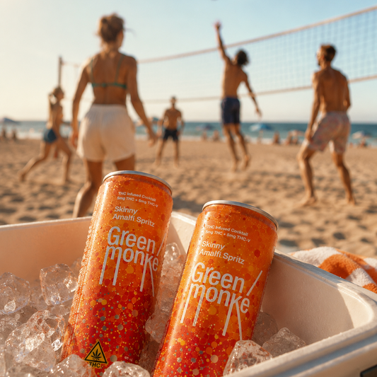 Two Green Monke Skinny Amalfi Spritz cans with THC and THCV, resting in ice inside a cooler on a beach with people playing volleyball in the background.